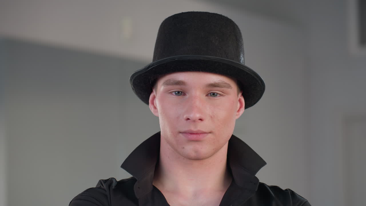 portrait of young man in black hat and shirt looking away with subtle smile inside loft studio with mirror background confident modern style vibe