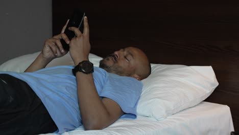 hombre descansando en una cama de hotel y agarrando el teléfono móvil para navegar sin rumbo
