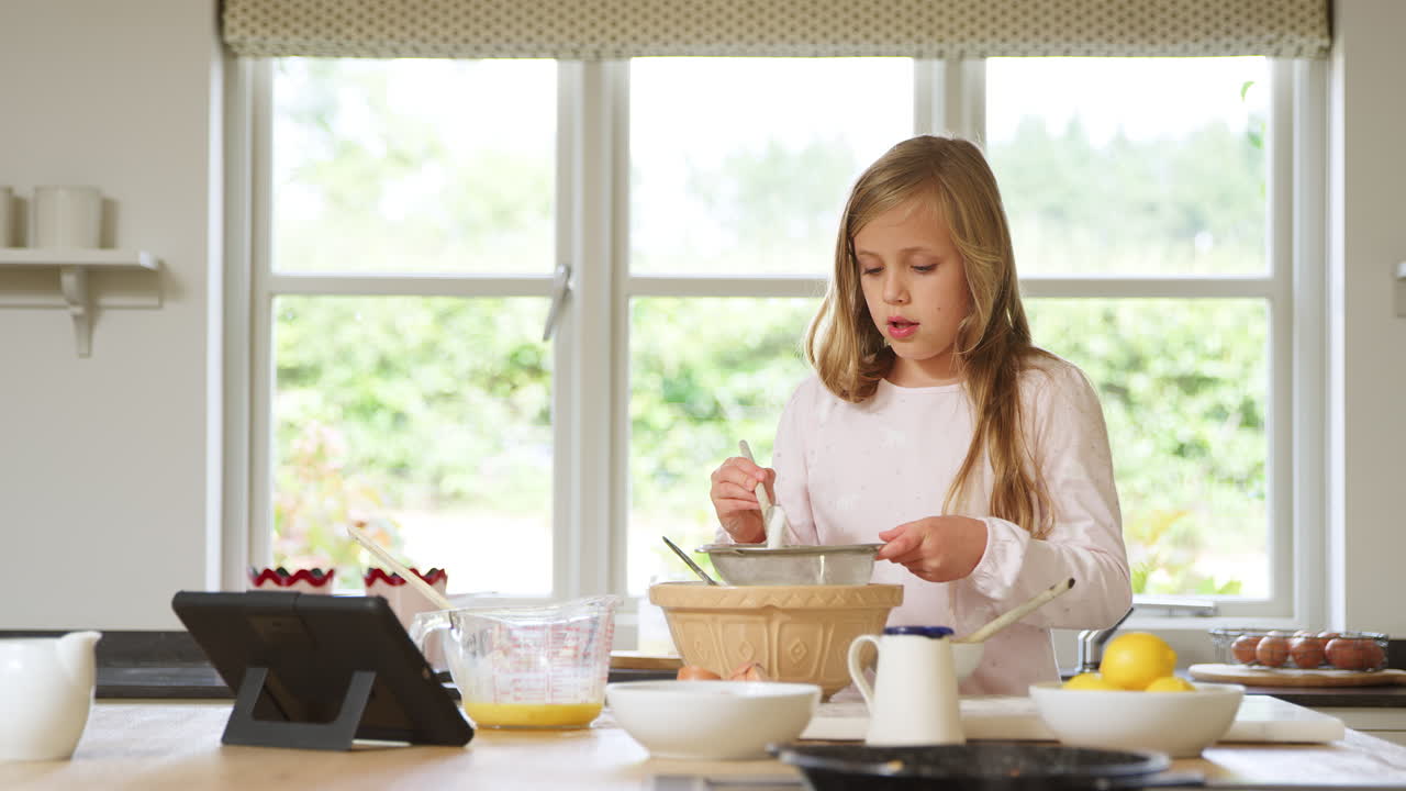 chica vestida con pijama horneando en la cocina en casa siguiendo la receta en una tableta digital