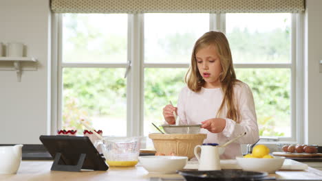 chica vestida con pijama horneando en la cocina en casa siguiendo la receta en una tableta digital