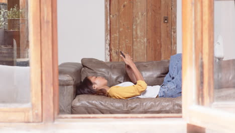 Relaxing on couch, asian young woman using smartphone comfortably at home