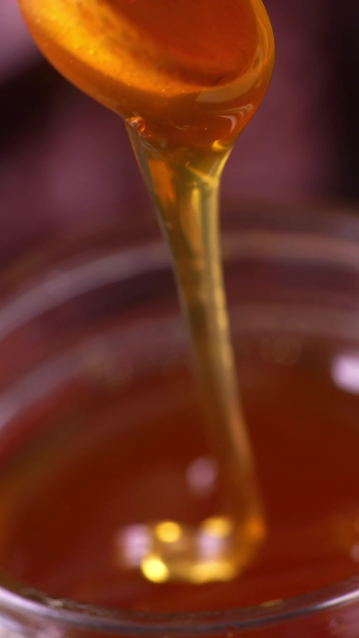 Primo piano di miele dorato che cola dolcemente da un cucchiaio in un barattolo sottostante. La consistenza ricca e lucida e le vibranti tonalità dorate mettono in risalto la dolcezza naturale e l'invitante viscosità
