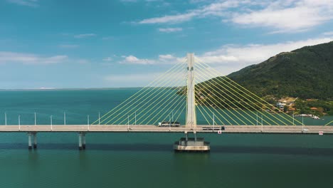 drone aerial side view of concrete cable-stayed bridge road above turquoise color ocean, located in laguna, santa catarina, brazil