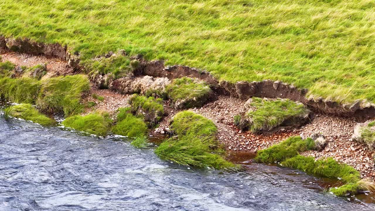 Slow camera pan reveals eroded grassy riverbank, flowing water, and tranquil rural landscape lighting