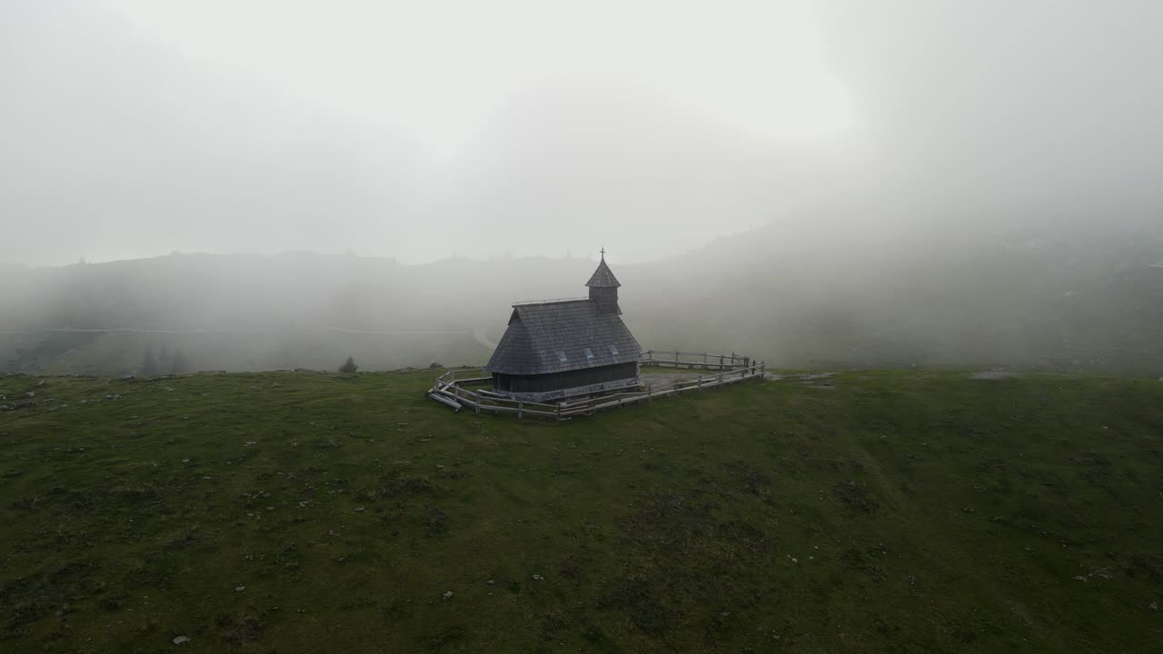 Tåkete kapell plassert på en gresskledd bakketopp i Velika Planina, Kamnik, Slovenia, flyfoto