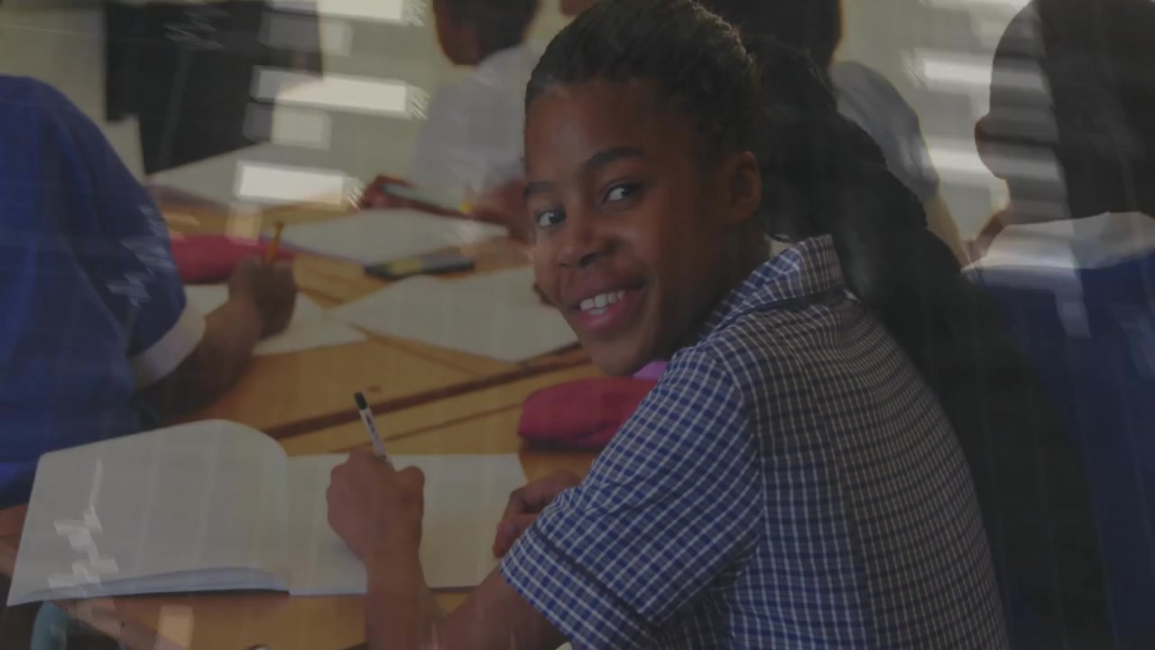 African American Schoolgirl Writing in Notebook in Classroom