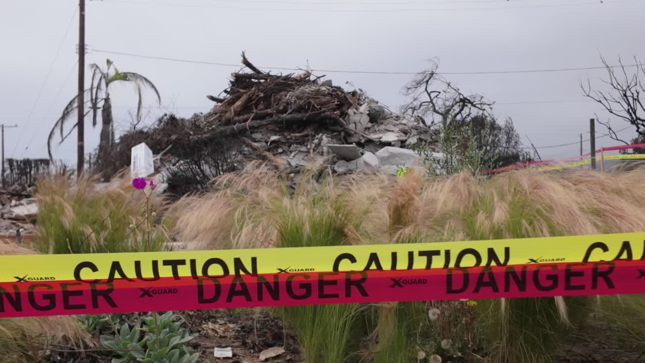 Gimbal close-up shot of caution tape quarantining off a burned property in Pacific Palisades after the wildfire in Southern California. 4K at 60 FPS Slow Motion