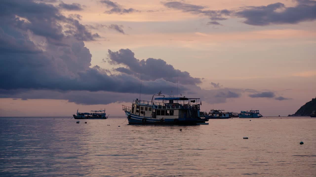 Boats anchored at sunset in Thailand, Ko Tao, under dramatic skies above calm waters