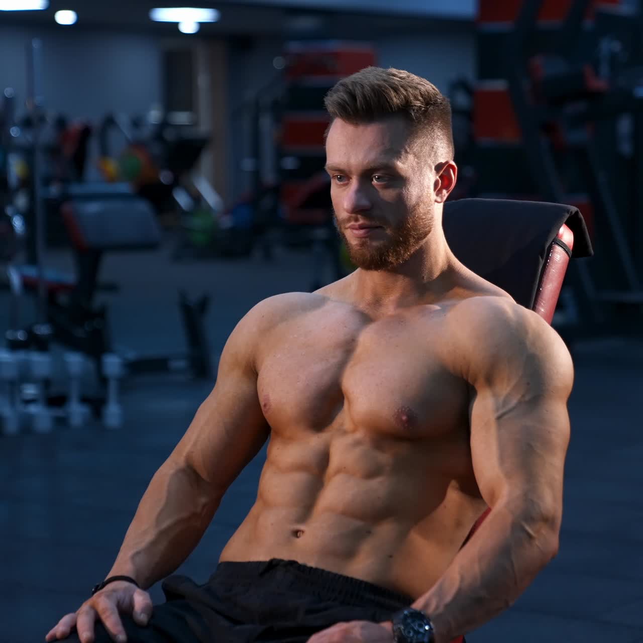 Handsome athletic man rests after heavy training in gym. Modern fitness gym background. Slow motion