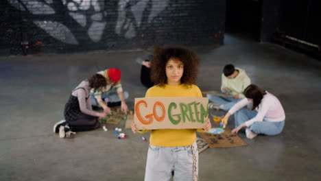 young environmental activist holding a cardboard with go green" inscription and looking at the camera"