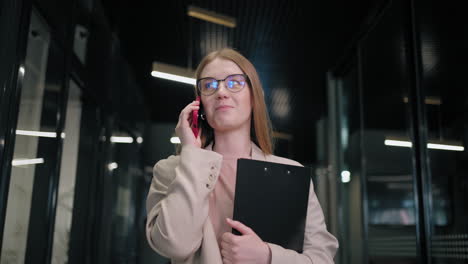 Porträt-Einer-Geschäftsfrau-Mit-Brille,-Die-Durch-Den-Büroflur-Geht-Und-Mit-Kunden-Telefoniert