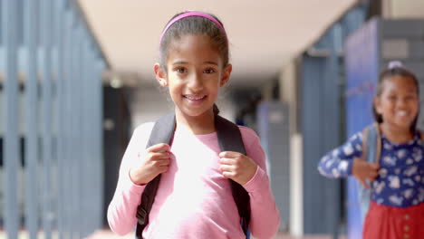 in school, two young biracial female students wearing backpacks are walking