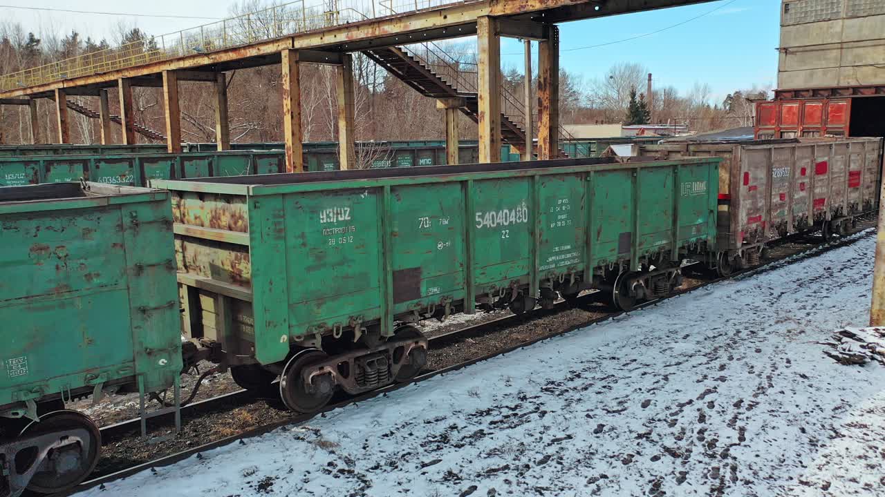 Empty containers are moving slowly on rails on the background of the cargo railway station under bridge at countryside. Aerial view.