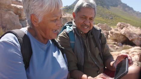 happy senior biracial couple in mountains taking selfie with smartphone, in slow motion