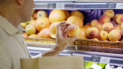 a middle-aged shot visitor selects peaches from a display case and puts them into a paper bag. eco-friendly packaging. daily