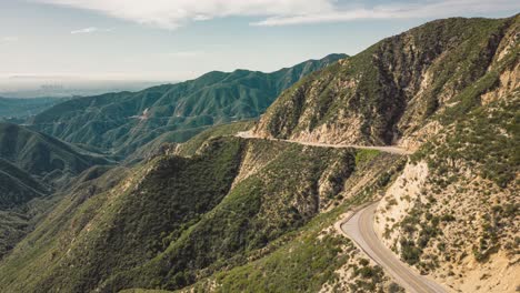 establish-drone-time-lapse-of-cars-on-winding-mountain-road-with-lush-greenery-and-Los-Angeles-skyline-in-the-background-cars-and-automobiles-hugging-the-sides-of-the-mountain-hills-crisis-crossing