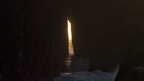 view through the zawn pyg rock arch in nanjizal beach at sunset in st levan, cornwall, uk