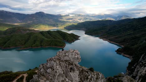 aerial of man sitting on a rock at bovilla lake near tirana in albania