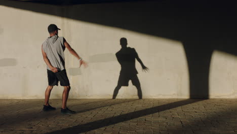 Tanzender-Mann,-Junger-Straßentänzer,-Breakdance,-Der-Verschiedene-Freestyle-Tanzbewegungen-Vorführt,-Geeigneter,-Gemischtrassiger-Mann,-Der-Bei-Sonnenuntergang-In-Der-Stadt-Mit-Schatten-An-Der-Wand-übt