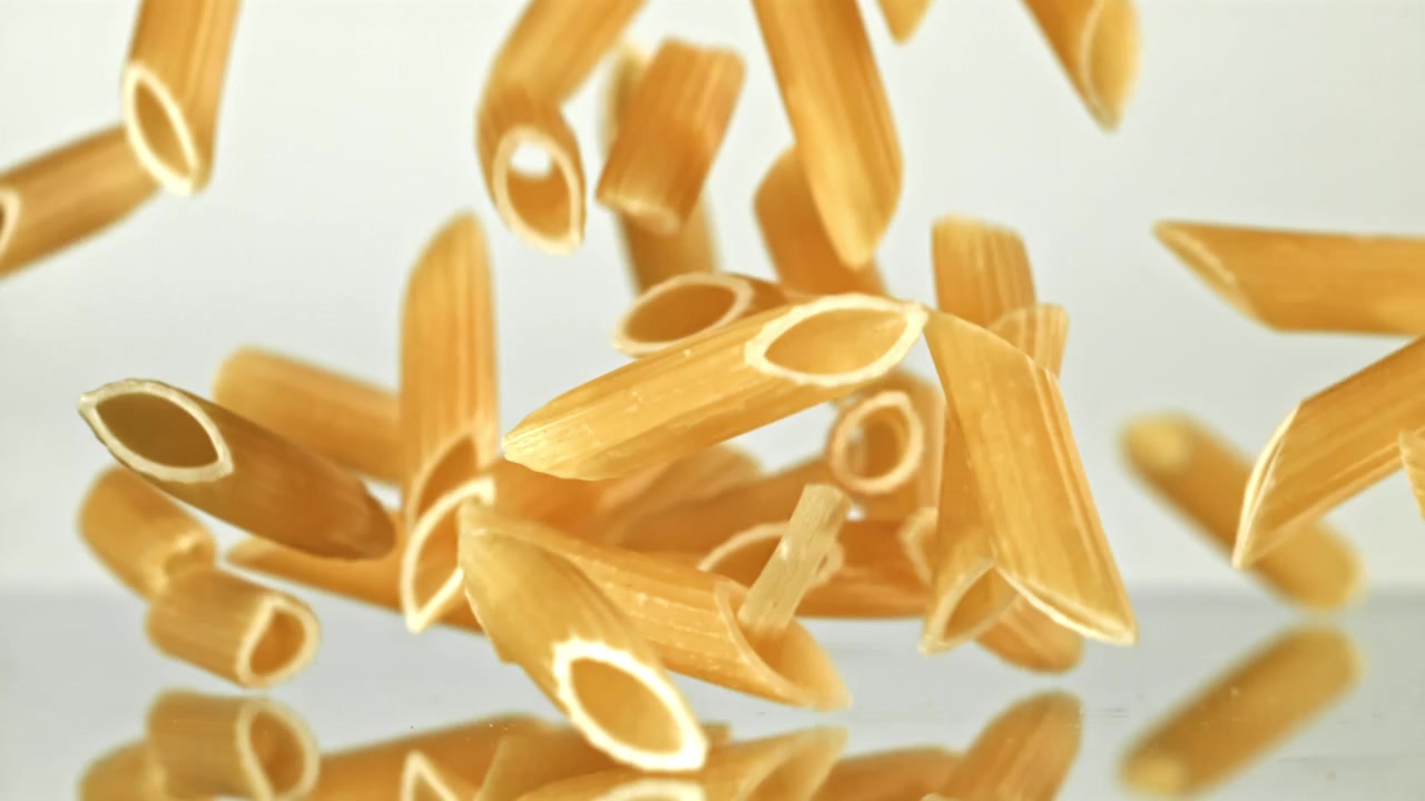 Penne che cadono al rallentatore su sfondo bianco
