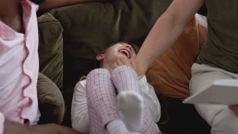 same sex male couple reading book with daughter at home together whilst tickling her