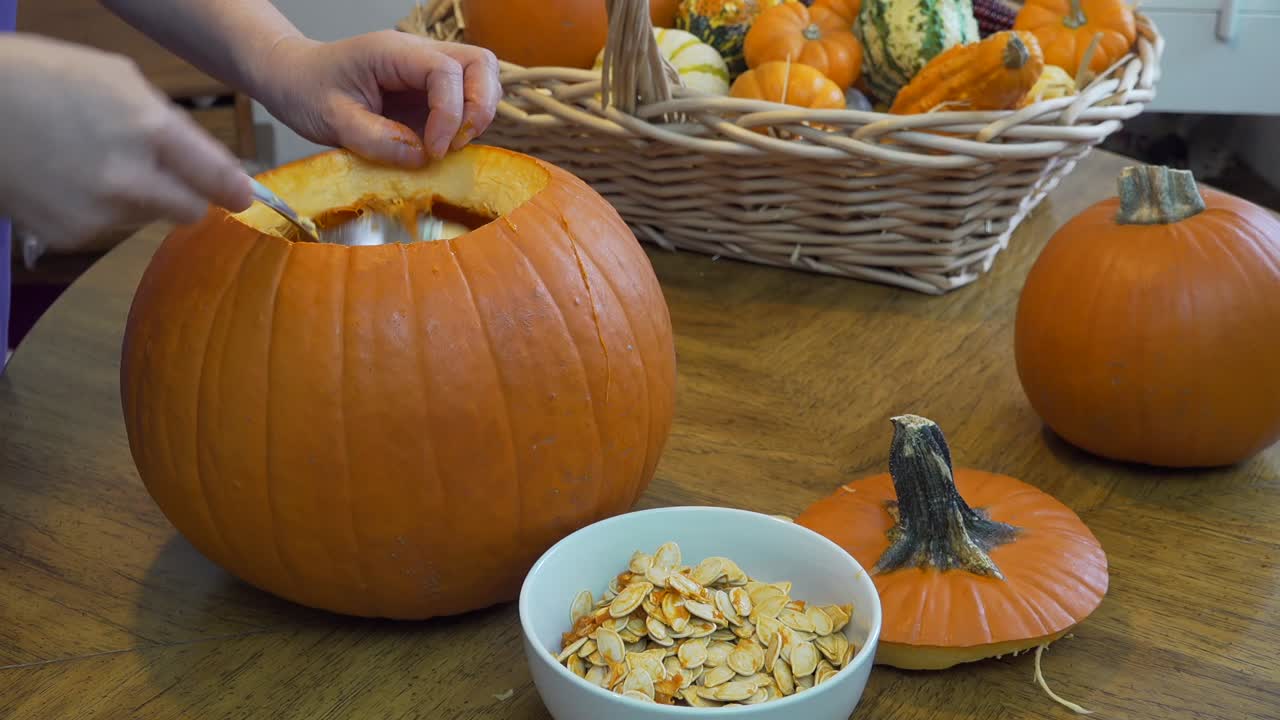 한 여성이 호박에서 씨를 긁어내고 옆면에서 자연 채광이 들어오는 식탁 위의 흰색 그릇에 넣는 클로즈업 샷