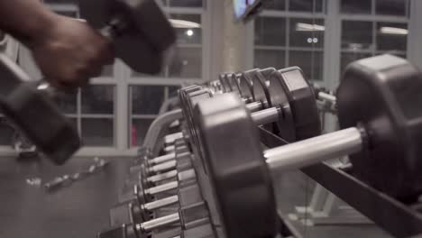 Black-man-picking-up-dumbbell-from-weight-rack-at-the-gym-for-workout,-close-up-shot