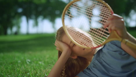 Blond-girl-lying-in-golden-sunlight-close-eyes.-Dreamy-cute-child-hold-racket