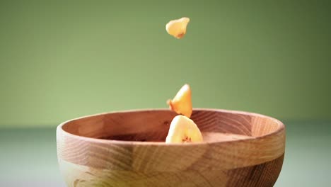 slow motion shot of dried fruits falling in wooden bowl in green background