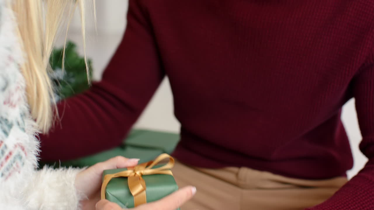 Exchanging gifts by Christmas tree, diverse couple sharing festive holiday moment together