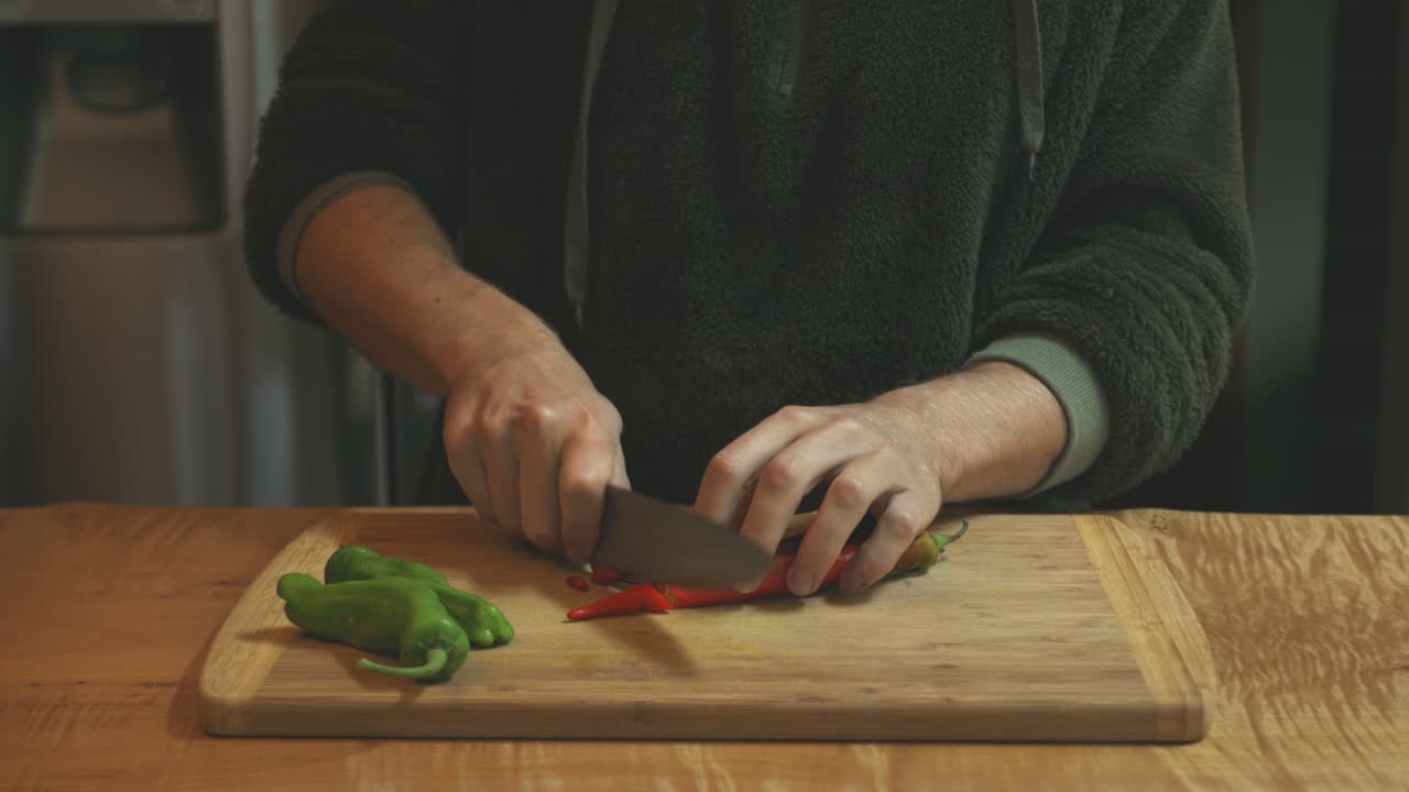 cocinero cortando pimienta picante roja y verde en la tabla de corte de alimentos de la cocina
