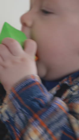 adorable little boy nibbles color toys standing at low wooden table with bright cubes by white wall extreme close view