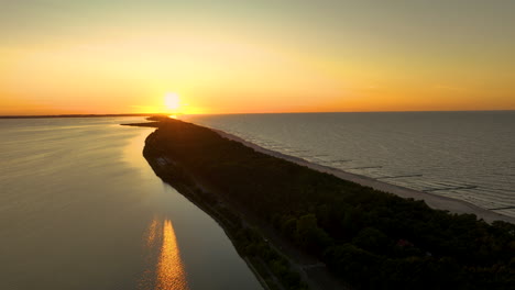 Aerial view of a sunset over a narrow strip of land between two bodies of water, with the sun reflecting on the water surface - Kuźnica