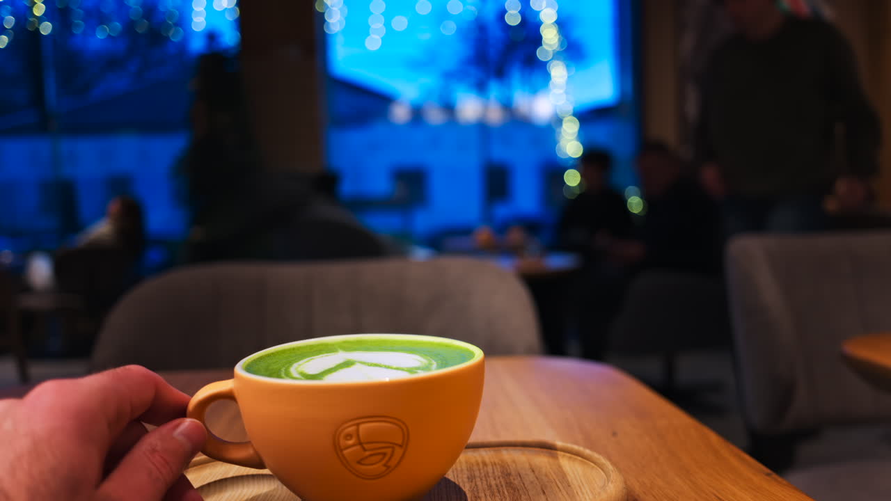 Close up of a man holding a cup of matcha latte on a wooden tray at a cafe