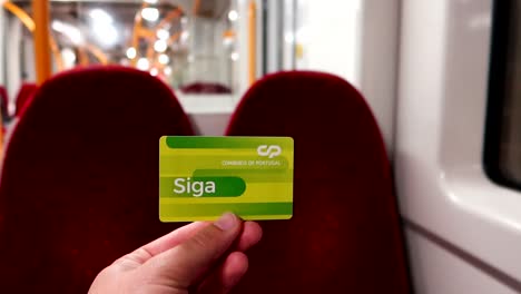 male hand holding portuguese green train card inside of an empty train passenger wagon