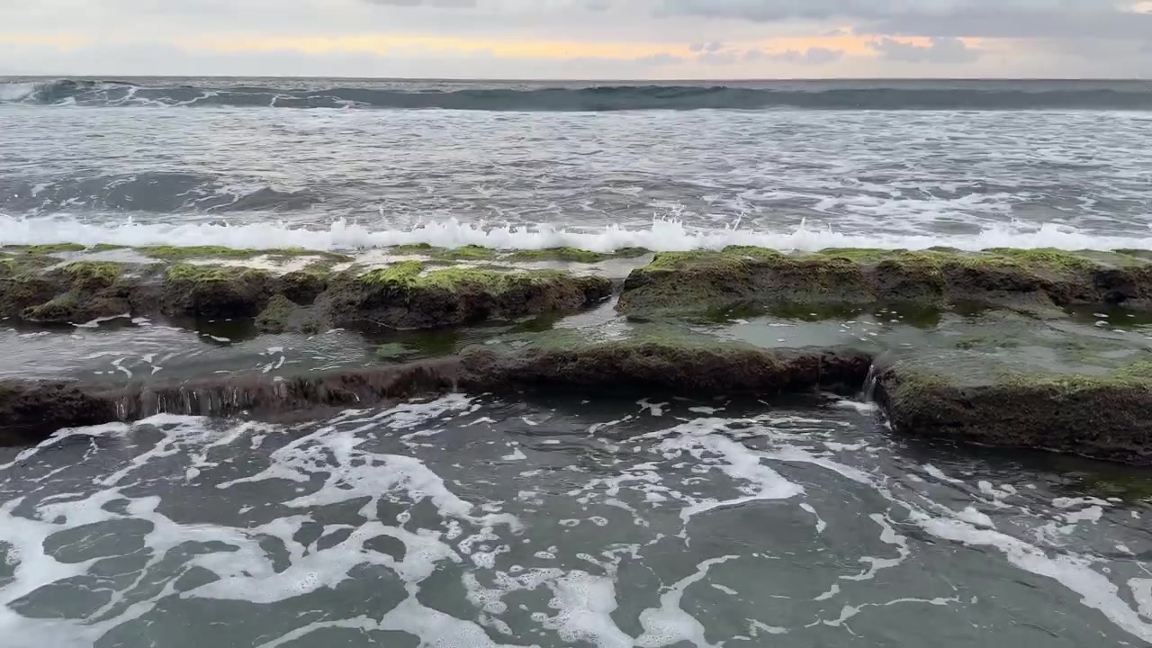 Onde dell'oceano che si infrangono e schiumano su rocce costiere ricoperte di muschio