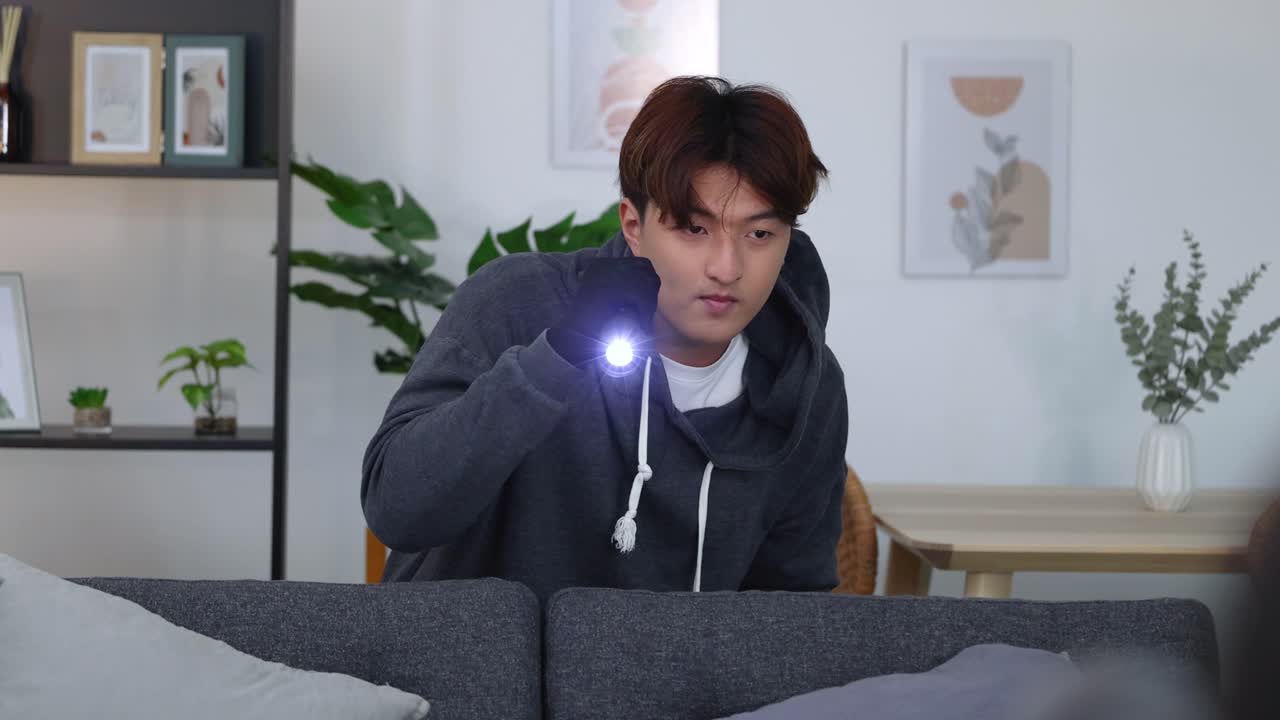フードと手袋を身に着けた男が、懐中電灯を使ってリビングを怪しげに調べています。