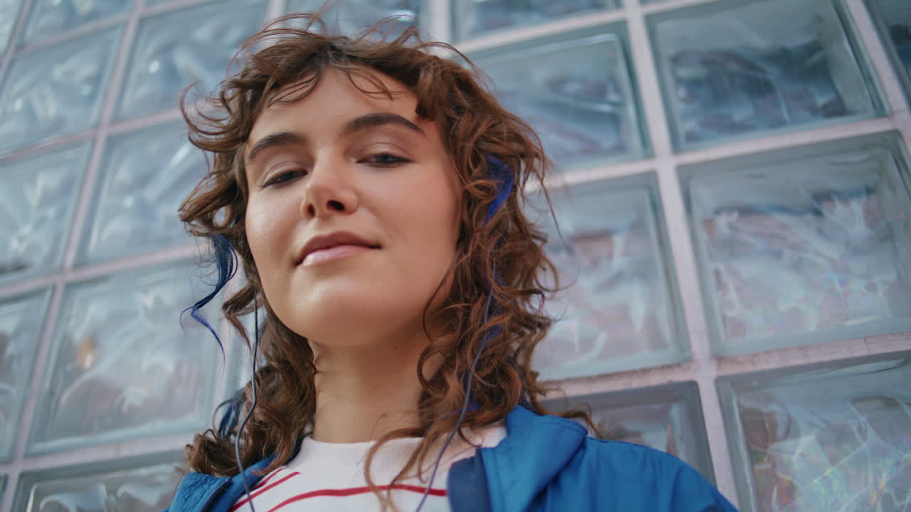 un melómano relajado escuchando música en auriculares apoyado en una pared de vidrio.