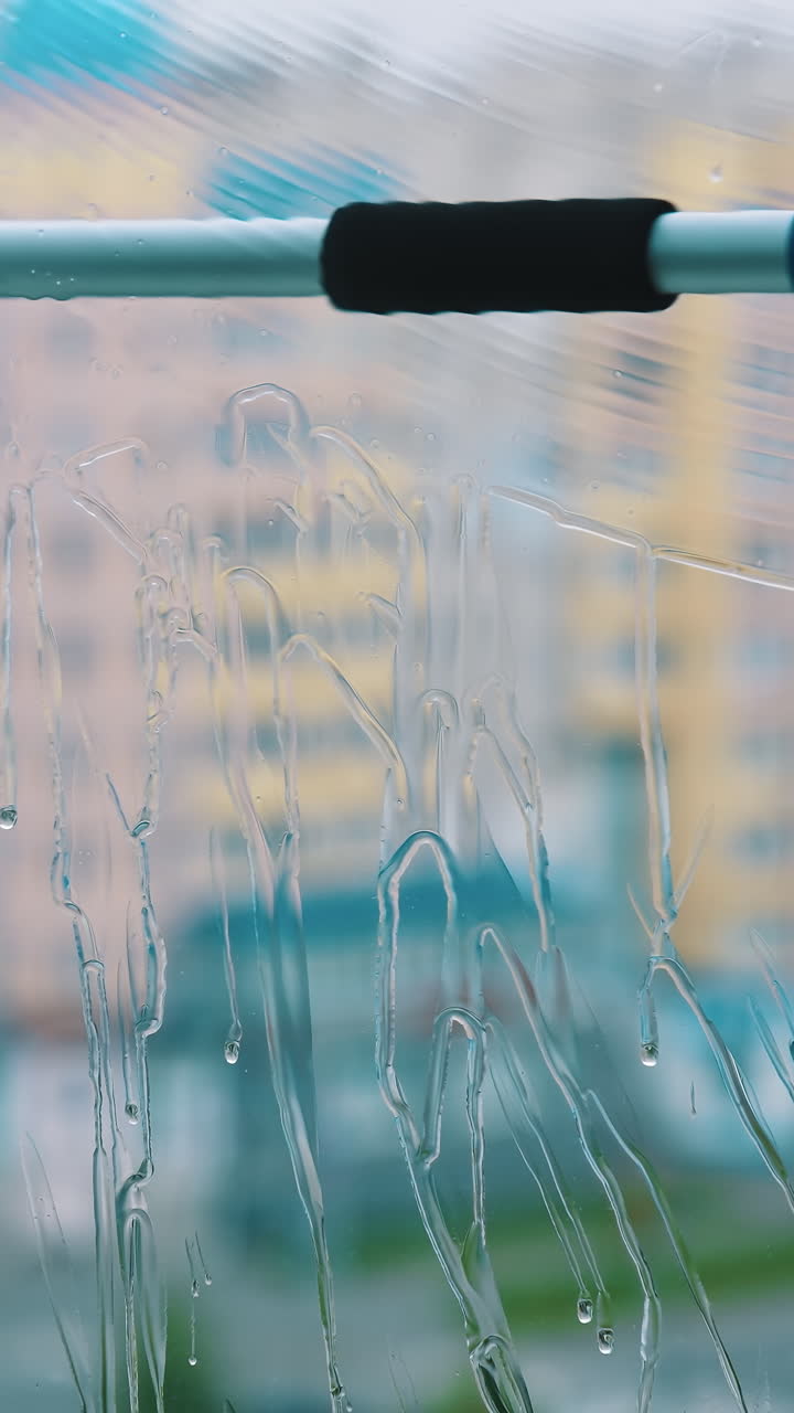 Window is cleaning with brush. Washing glass with clean water by special tool inside the flat. Professional window cleaning service. Close-up. Vertical video