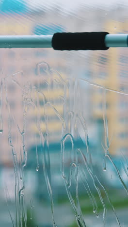 window is cleaning with brush. washing glass with clean water by special tool inside the flat. professional window cleaning service. close-up. vertical video