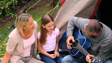 father playing guitar with wife and children singing in garden