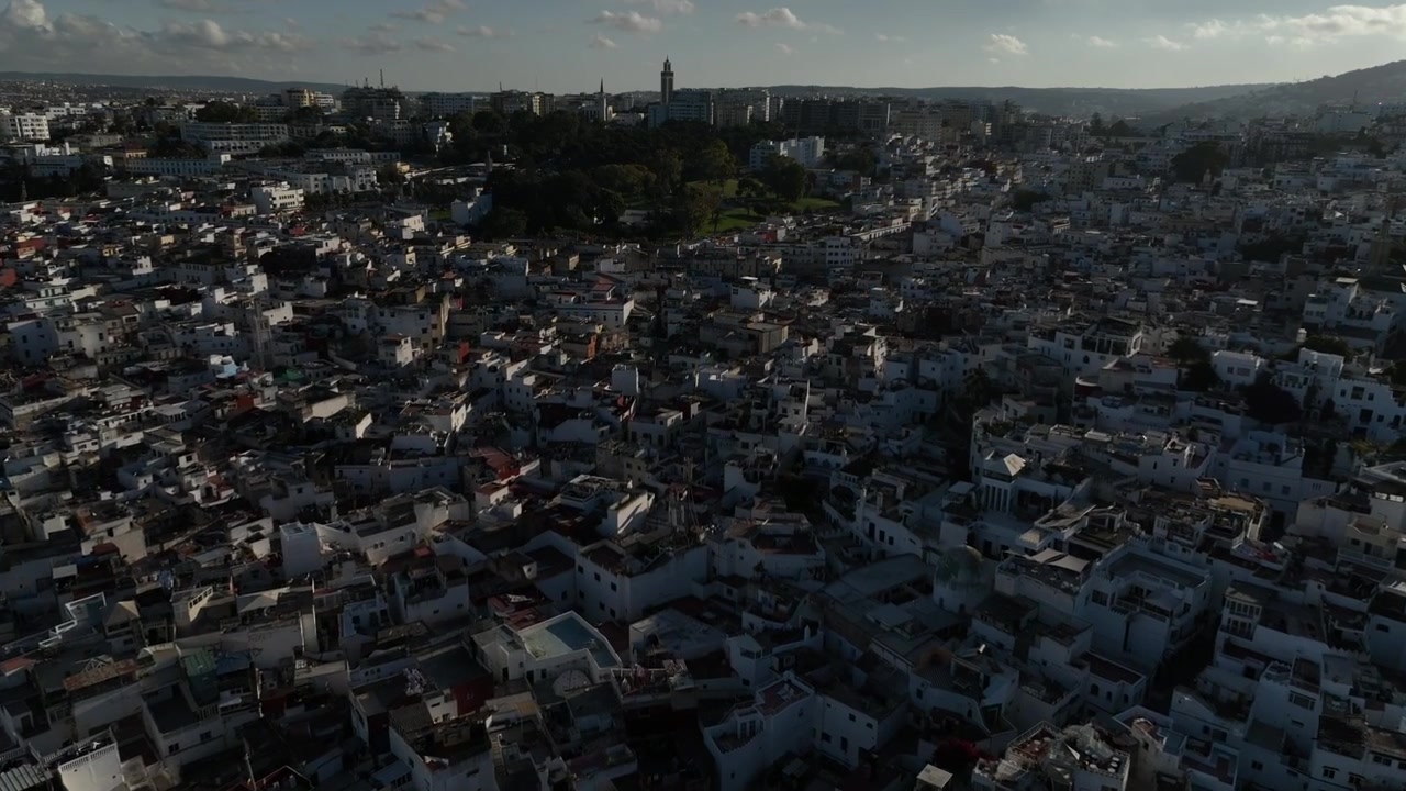 Ampia vista aerea di fitti quartieri bianchi che si estendono su una città collinare nel Marocco settentrionale, che rivela il tessuto urbano tradizionale, il minareto di una moschea e la caratteristica architettura nordafricana.