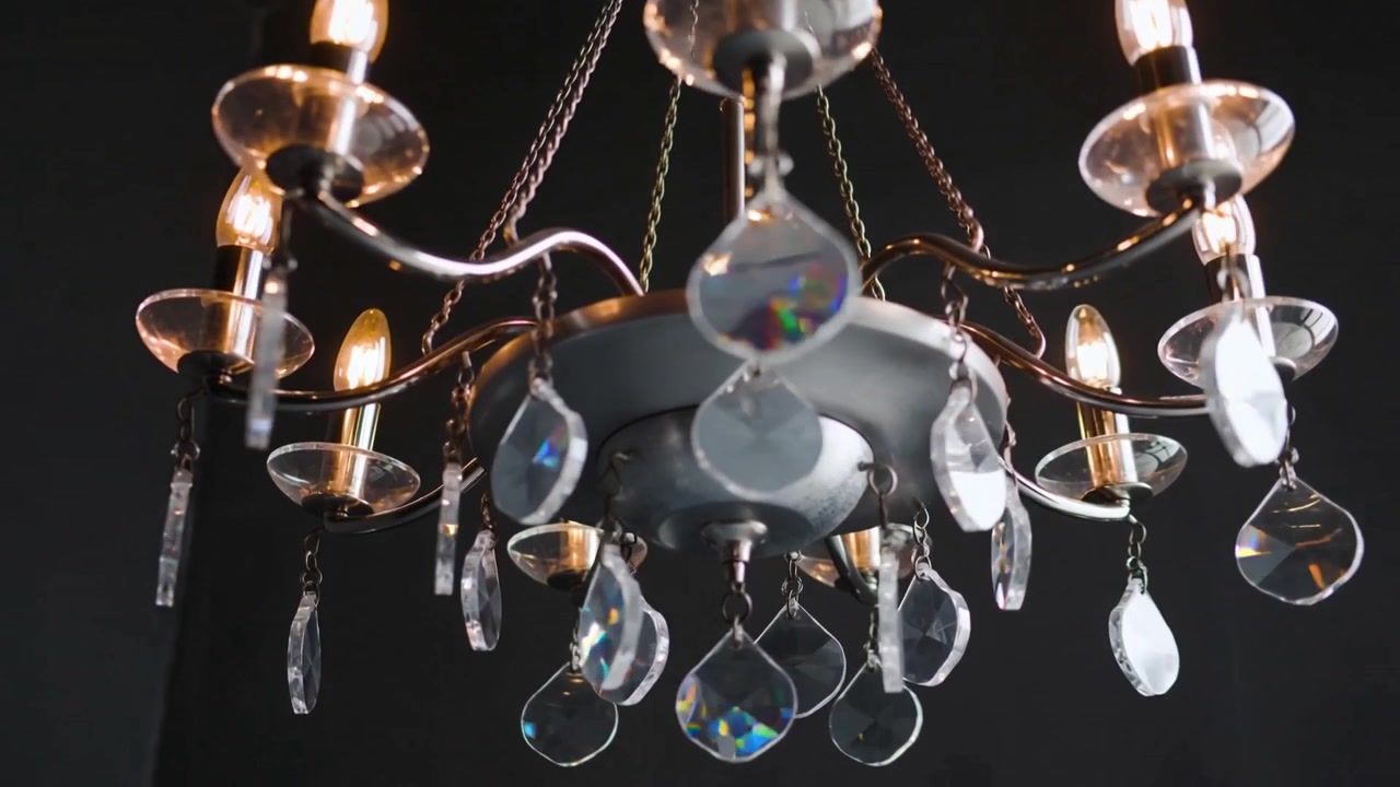 Telecamera che si muove verso un lampadario di cristallo in studio, rivelando lampadine accese e prismi per i dettagli.
