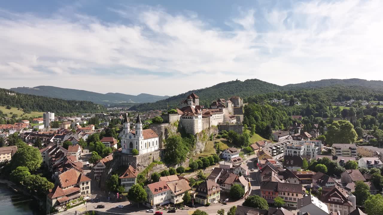 Aerial view captures the historic town of Aarburg in Switzerland, showcasing its prominent castle perched on a hill above the Aare River. The town's traditional buildings are nestled in a valley