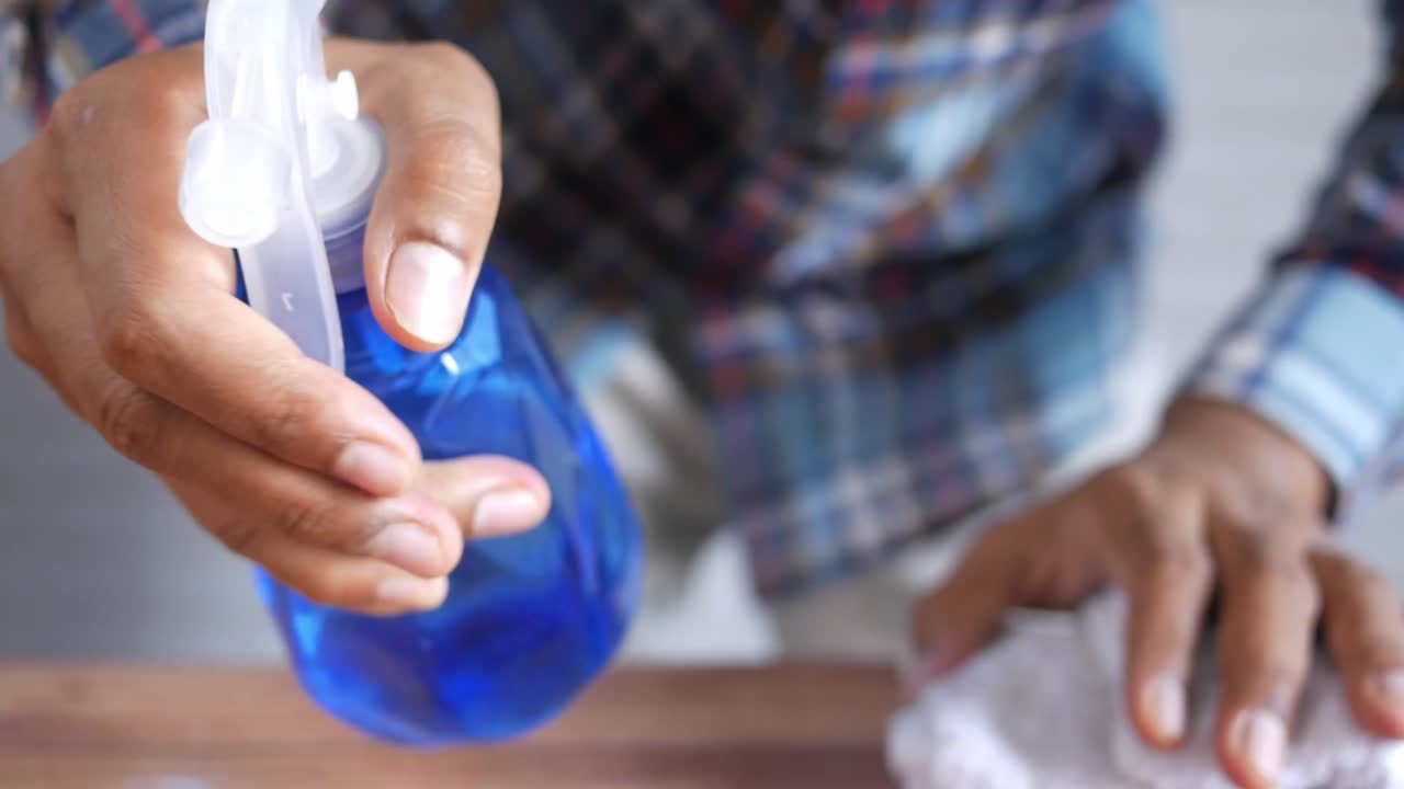 persona limpiando una mesa con una botella de spray y un paño