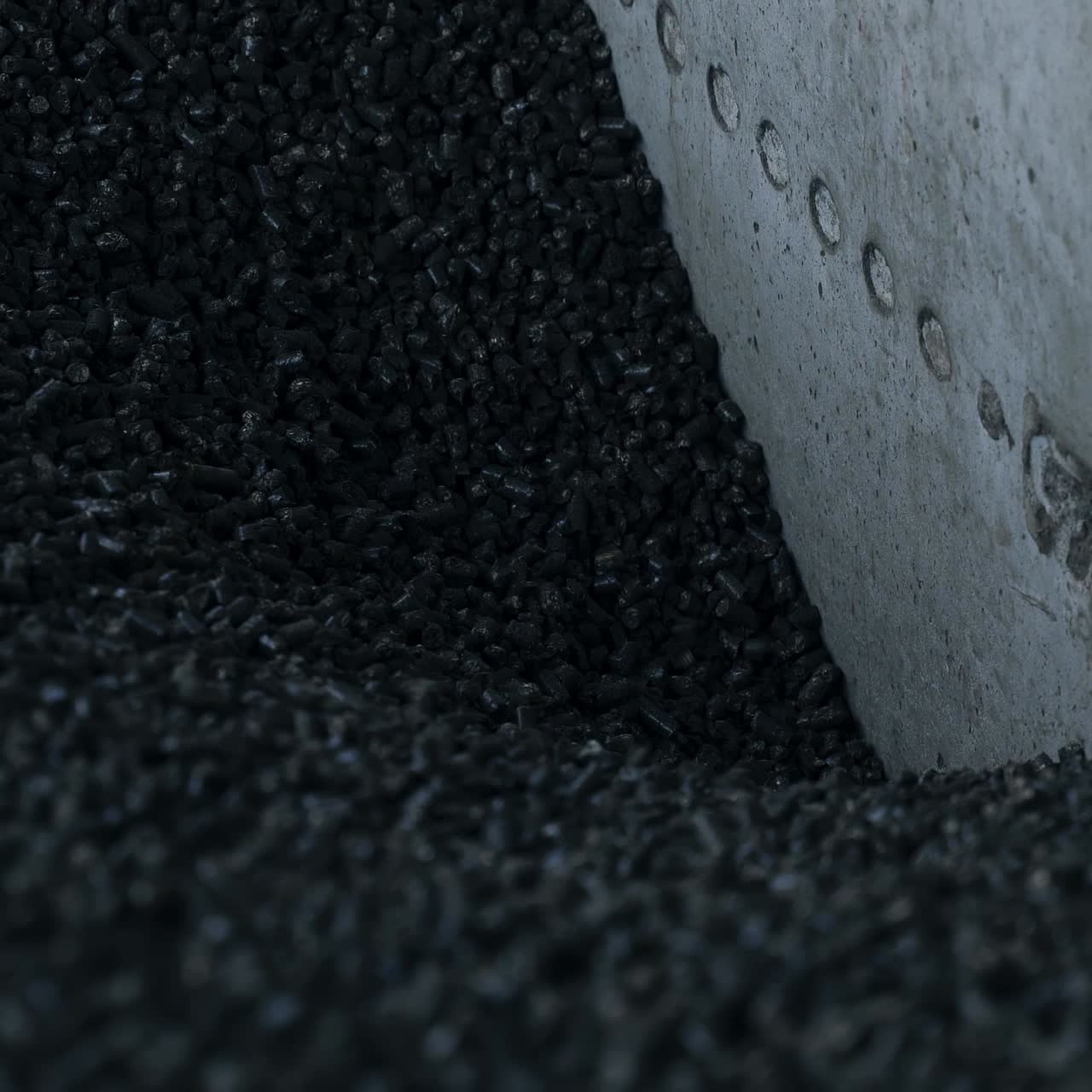 Heap of pressed charcoal moving downward into the furnace. Small pieces of pressed charcoal going down at the cement wall. Close up