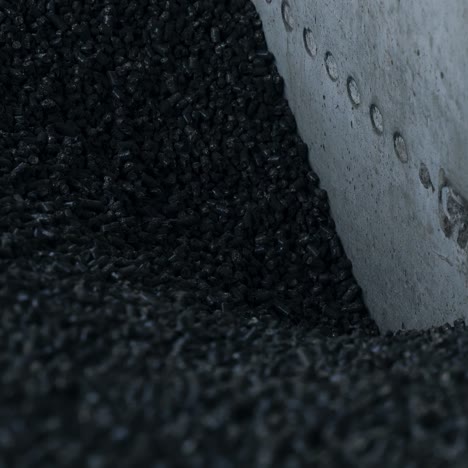 heap of pressed charcoal moving downward into the furnace. small pieces of pressed charcoal going down at the cement wall. close up