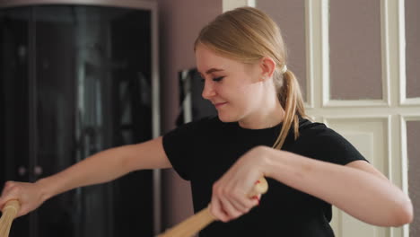 massage therapist in black outfit dances joyfully while using bamboo broom on client, standing near white panel door in warmly lit spa room with modern decoration and relaxed atmosphere