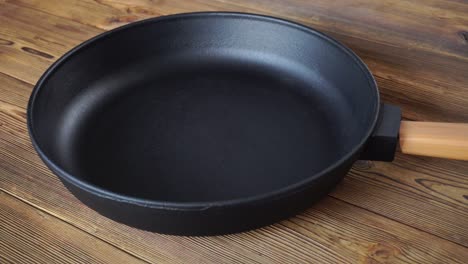 cast iron frying pan with removable wooden handle on wooden background. long lasting cooking pan for all types of stoves, domestic, kitchen