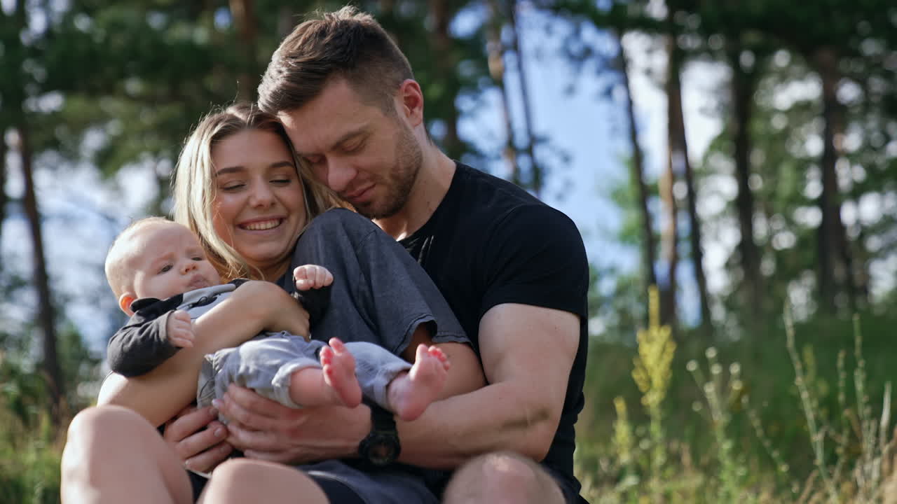 Family portrait of a happy Caucasian people. Couple sit in the nature on sunny day with their tiny baby.